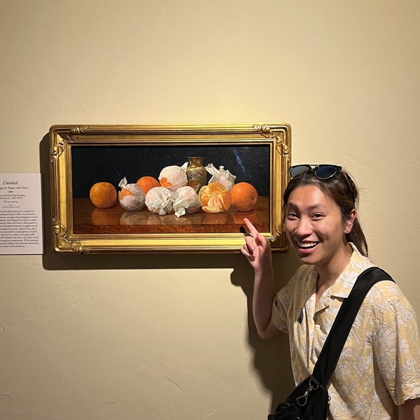 A picture of Ashley pointing at a painting of oranges.